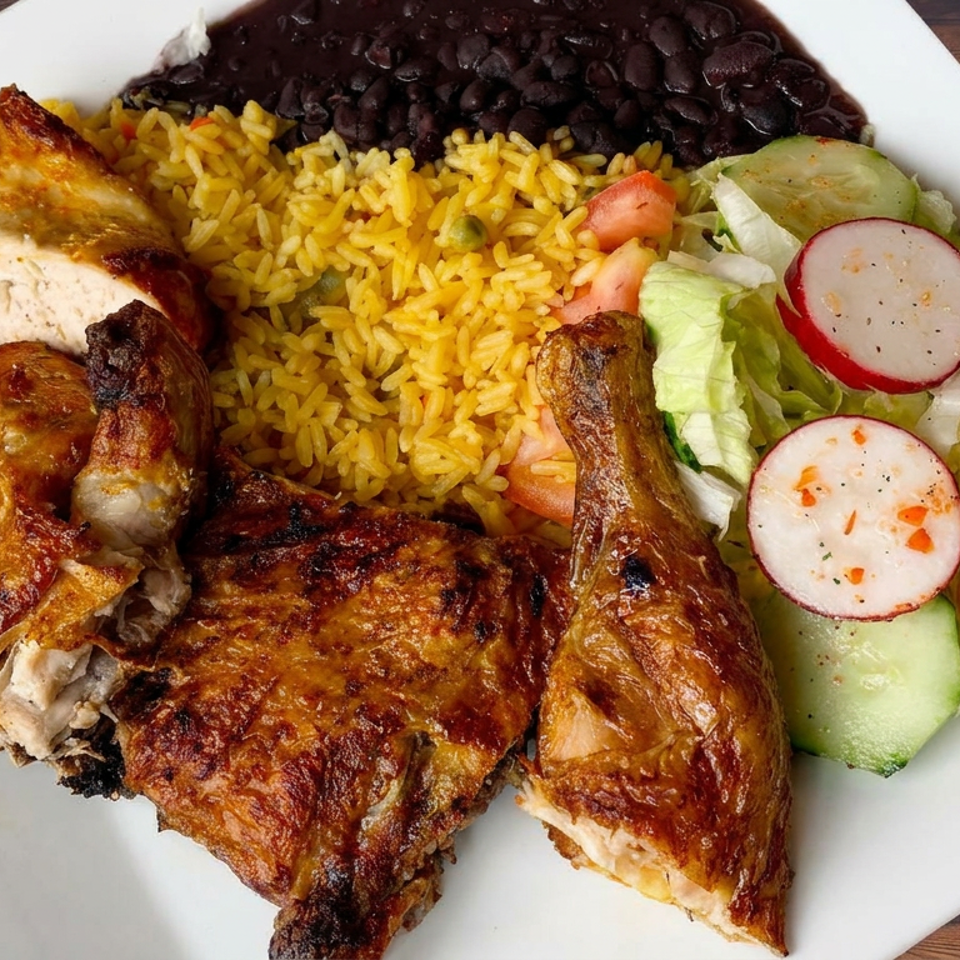 Plate of grilled chicken with yellow rice, black beans, and lettuce salad with tomato, cucumber, and radishes.