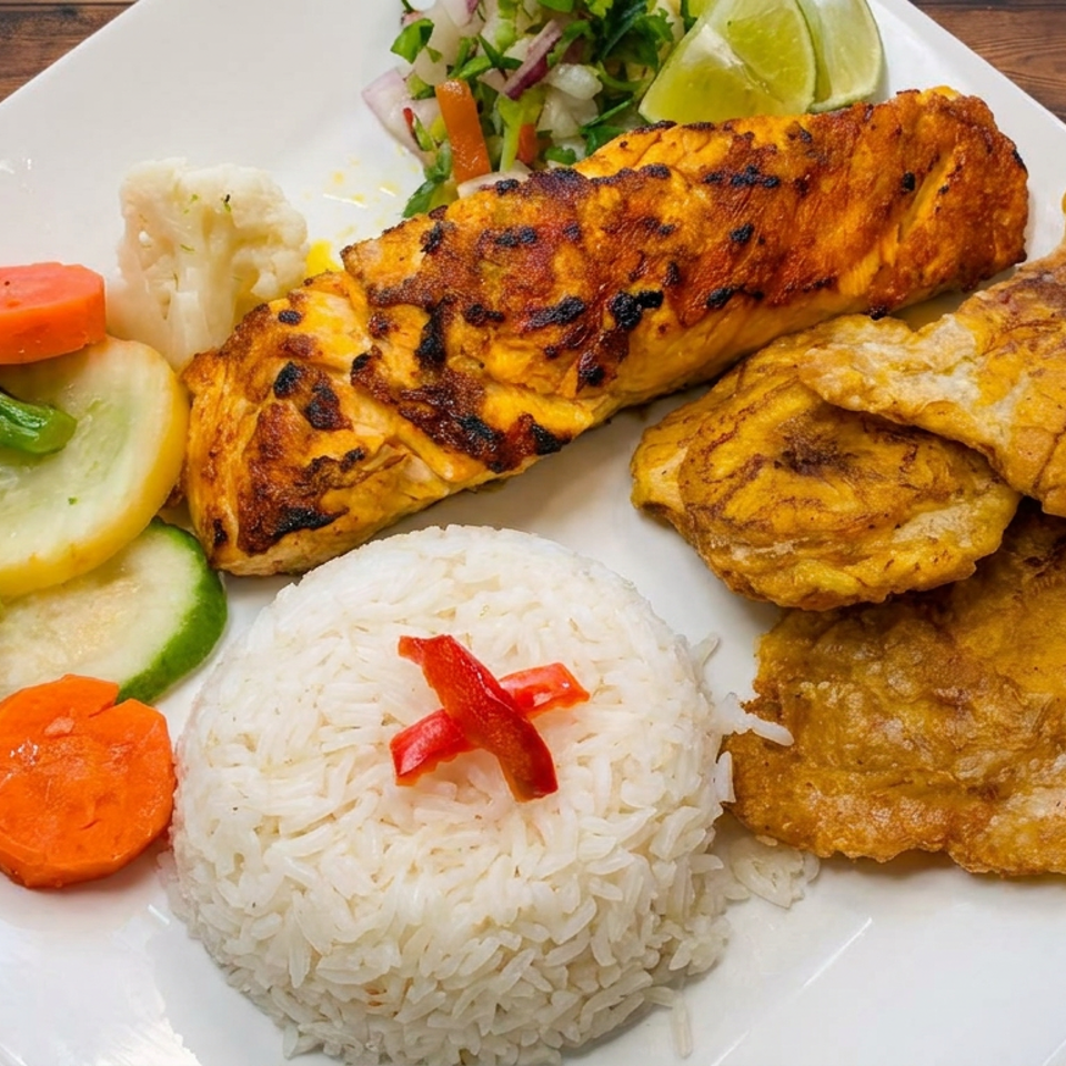 Grilled salmon, fried plantains, white rice, steamed vegetables, and lime garnish arranged on a white plate.